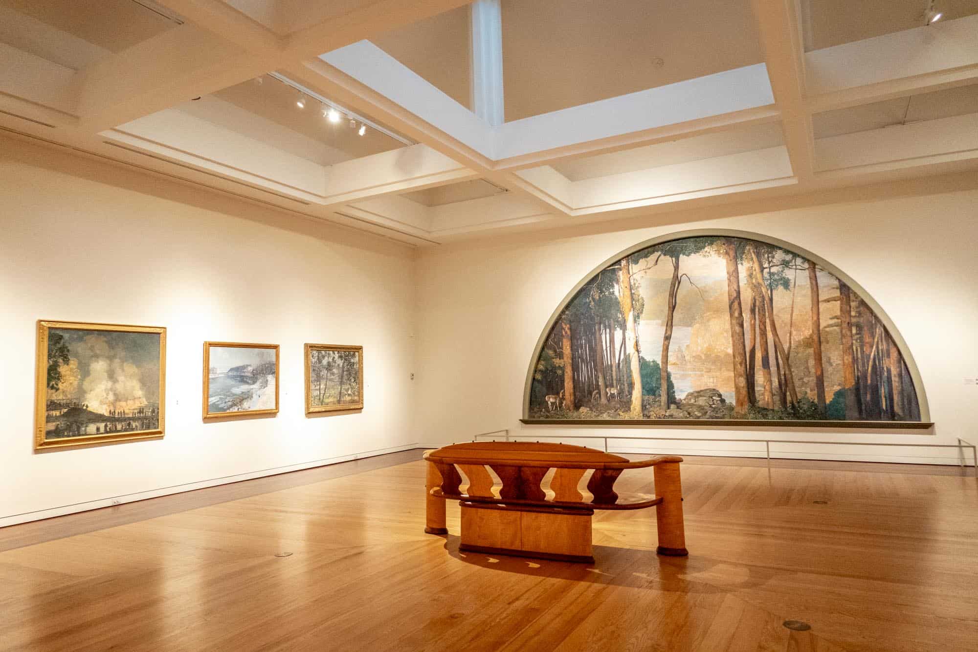 Four paintings, including one semi-circular woodland scene, on the walls of the Michener Art Museum