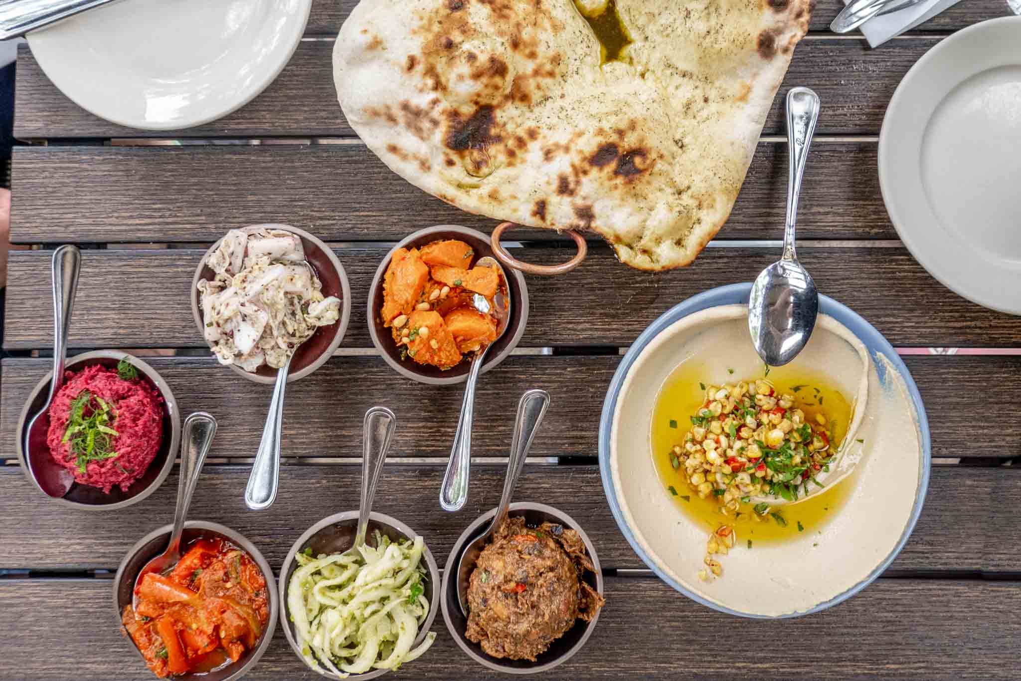 Table with an assortment of meze, a bowl of hummus, and flatbread.