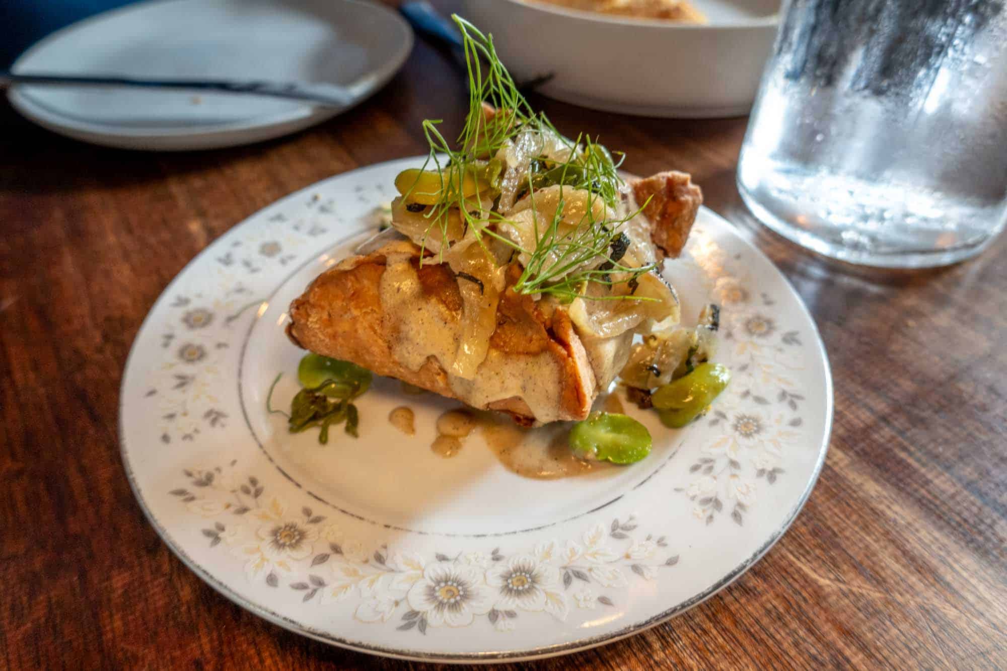 A samosa topped with sauce and dill fronds on a plate.