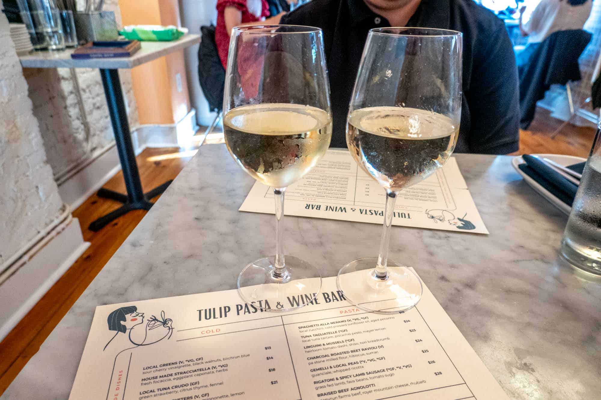 Two glasses of white wine on a table with a menu saying "Tulip Pasta & Wine Bar"